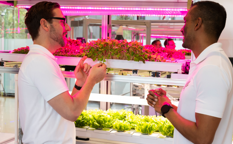 Nadun Hennayaka, CEO & Founder, and Michael Bridges, Market Research Analyst Standing in front of modular System growing leafy green plants