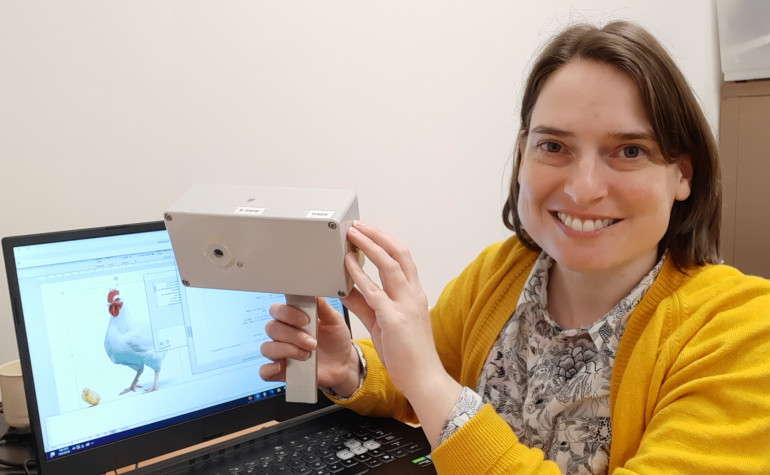 Dr Cheryl McCarthy holding camera technology in front of a computer screen with an image of a chicken on it